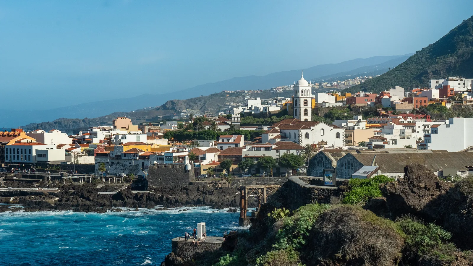 A view of Garachico, Tenerife: the town with the Iglesia de Santa Ana, the black volcanic-rock coast and the Atlantic, below the slopes of the valley
