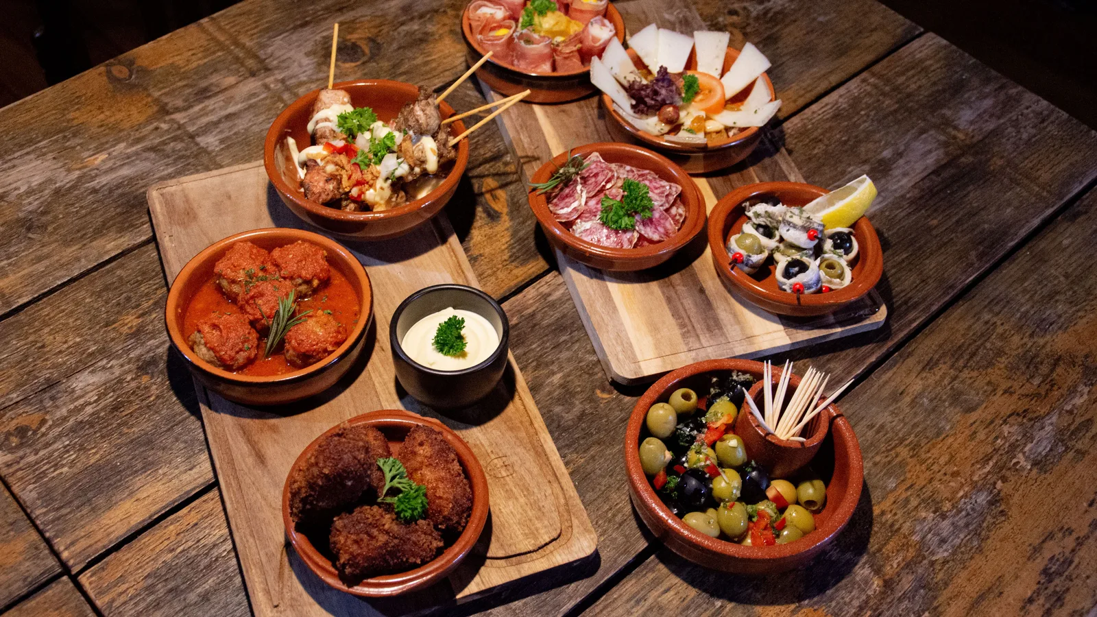 Tapas spagnole da condividere su tavolo rustico a Tenerife: olive, polpette, croquetas, salumi e formaggio in cazuelas di terracotta