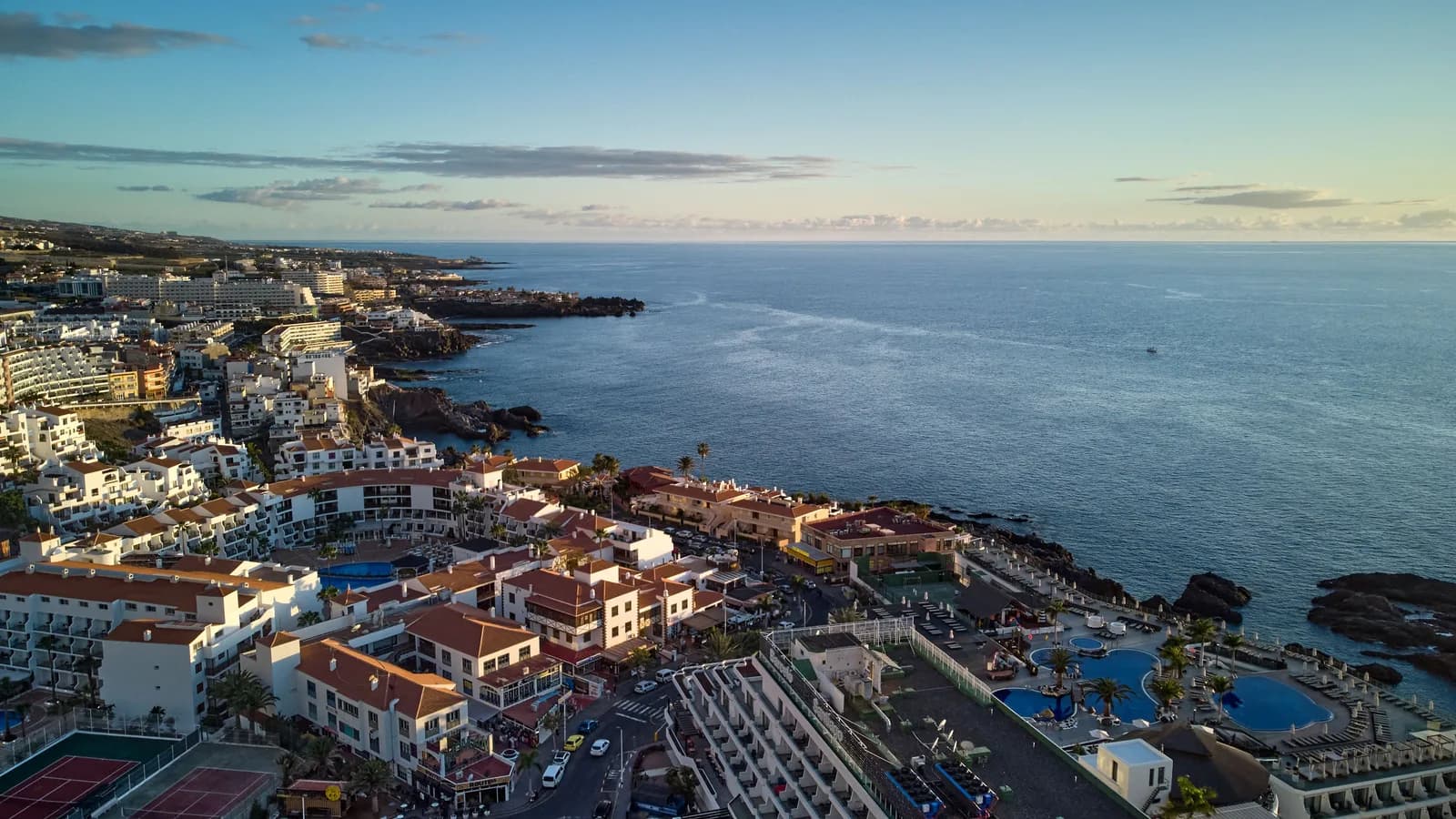 Vista aérea de una localidad de la costa suroeste de Tenerife (Puerto de Santiago) al atardecer, con hoteles, piscinas y costa volcánica frente al océano