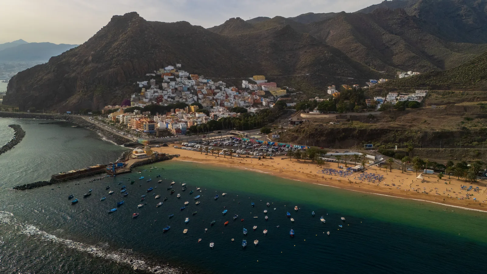 Vista de Playa de las Teresitas en Tenerife: arco de arena dorada, agua tranquila, palmeras y las montañas de Anaga al fondo