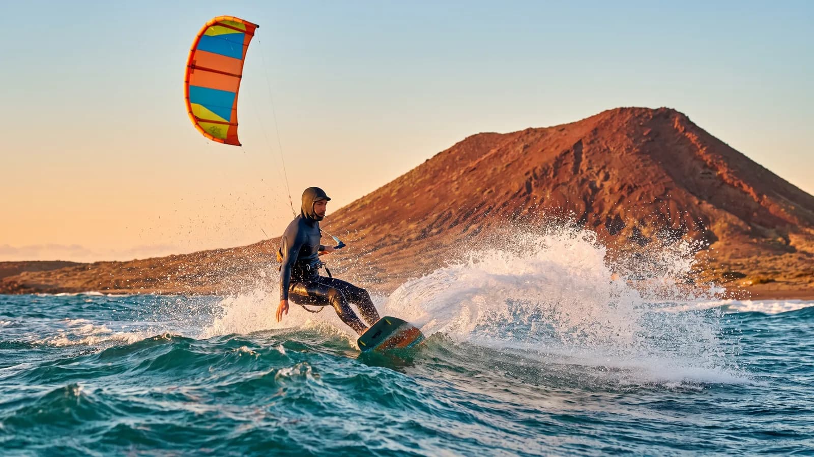 Kitesurfista sobre las olas en El Médano, Tenerife, con la Montaña Roja al fondo