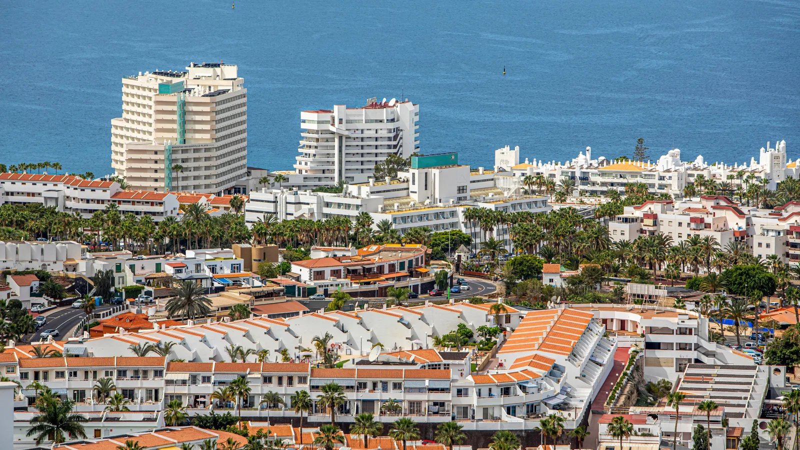 Vista aérea de la zona turística del sur de Tenerife: edificios blancos con tejados anaranjados, palmeras y el océano Atlántico al fondo