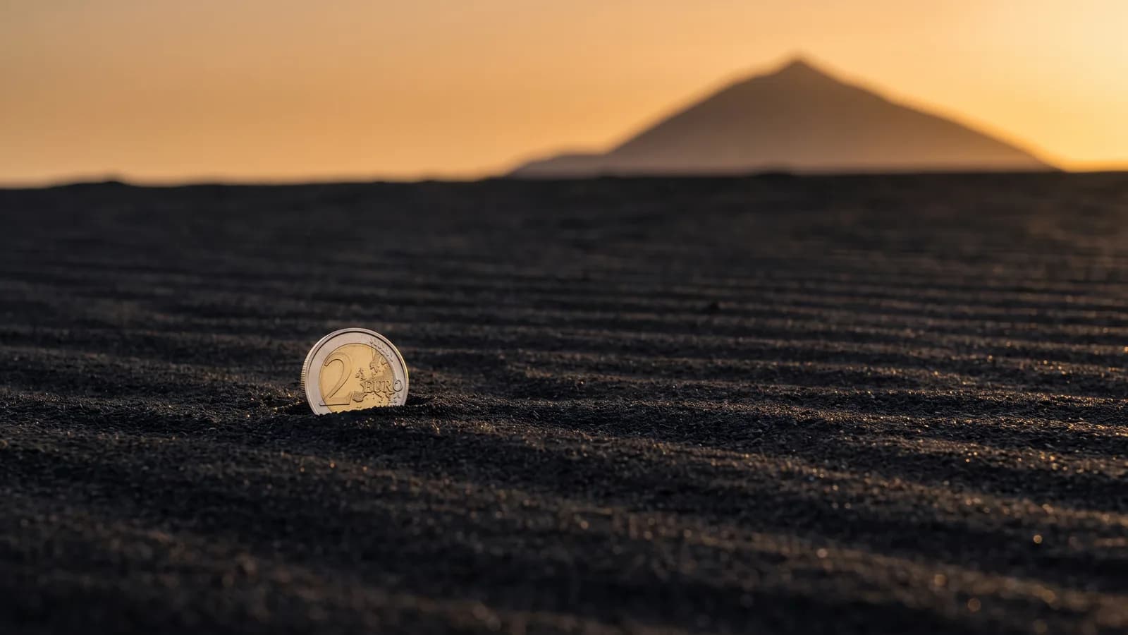 Moneda de 2 euros en la arena negra volcánica de Tenerife al atardecer, con el Teide desenfocado al fondo: cuánto cuesta de verdad la isla