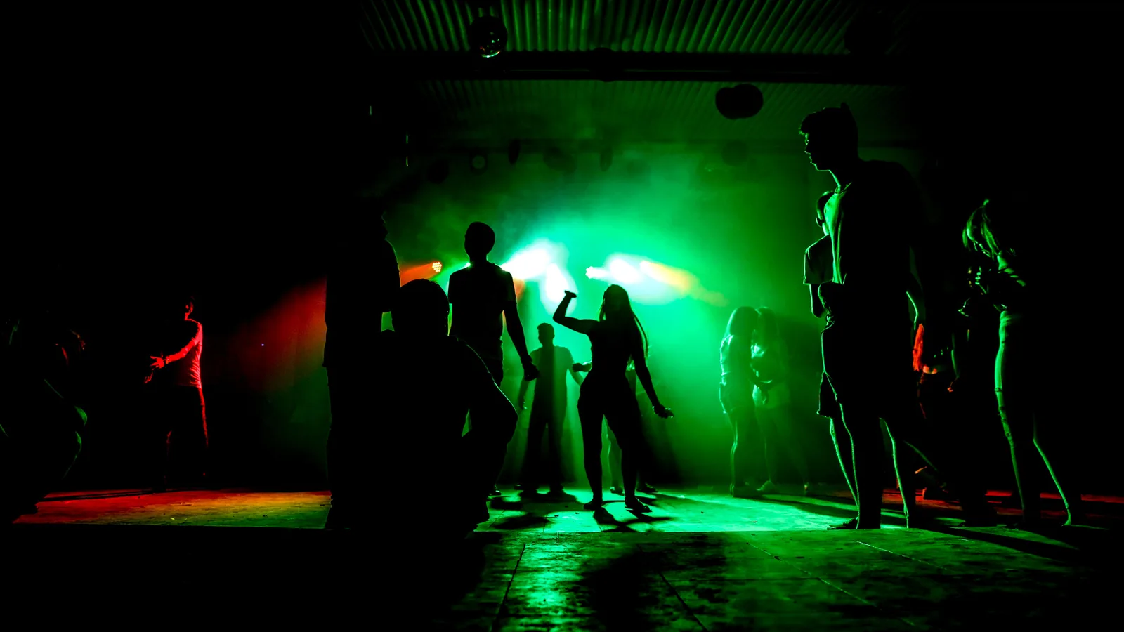 Siluetas de personas bailando en una discoteca con luces verdes y humo en el sur de Tenerife